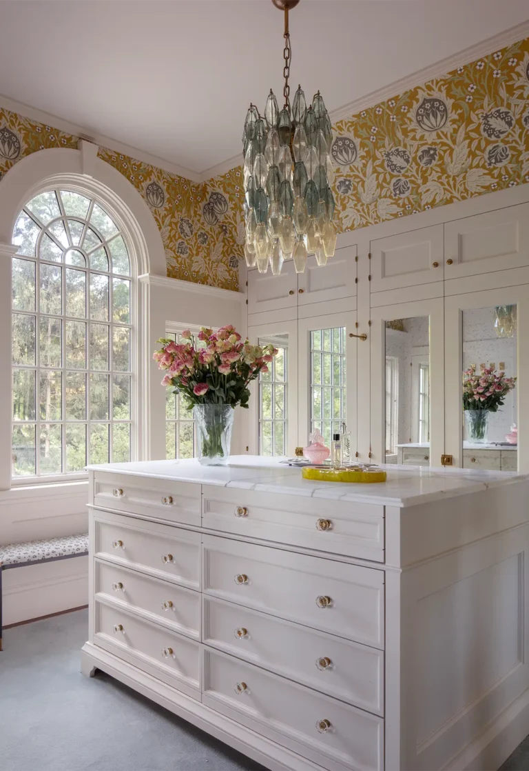 Dressing room with white cabinetry, arched window, chandelier, and marble-topped island