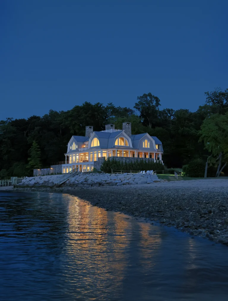Evening view of a Huntington Bay waterfront home glowing with interior light along the shoreline.