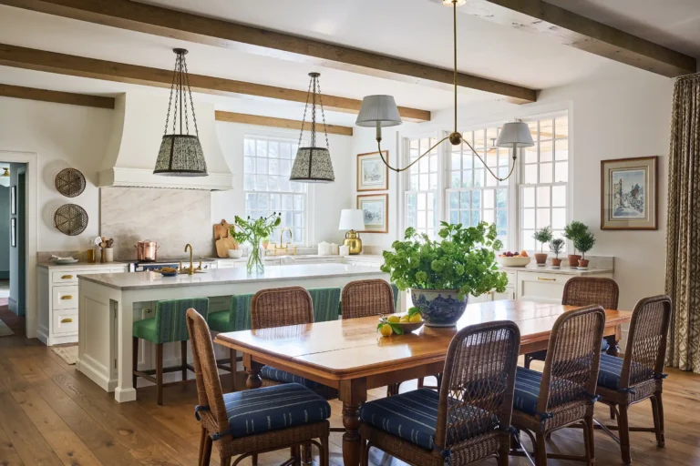 Cape Dutch residence great room with dining table, white kitchen cabinetry, exposed oak beams, and large windows in Matinecock