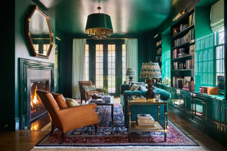 Deep green study library with fireplace, built-in bookcases, writing desk, upholstered seating, and tall windows