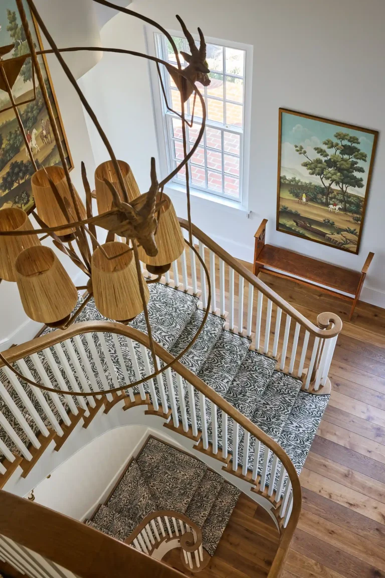 Main stair in Cape Dutch residence with curved railing, patterned stair runner, brass chandelier, and framed artwork