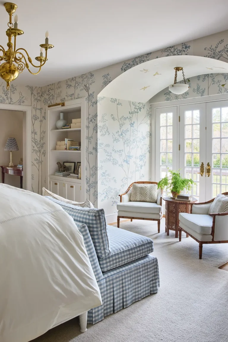 Primary bedroom with arched sitting bay, built-in shelves, pale patterned wallpaper, and upholstered seating by windows