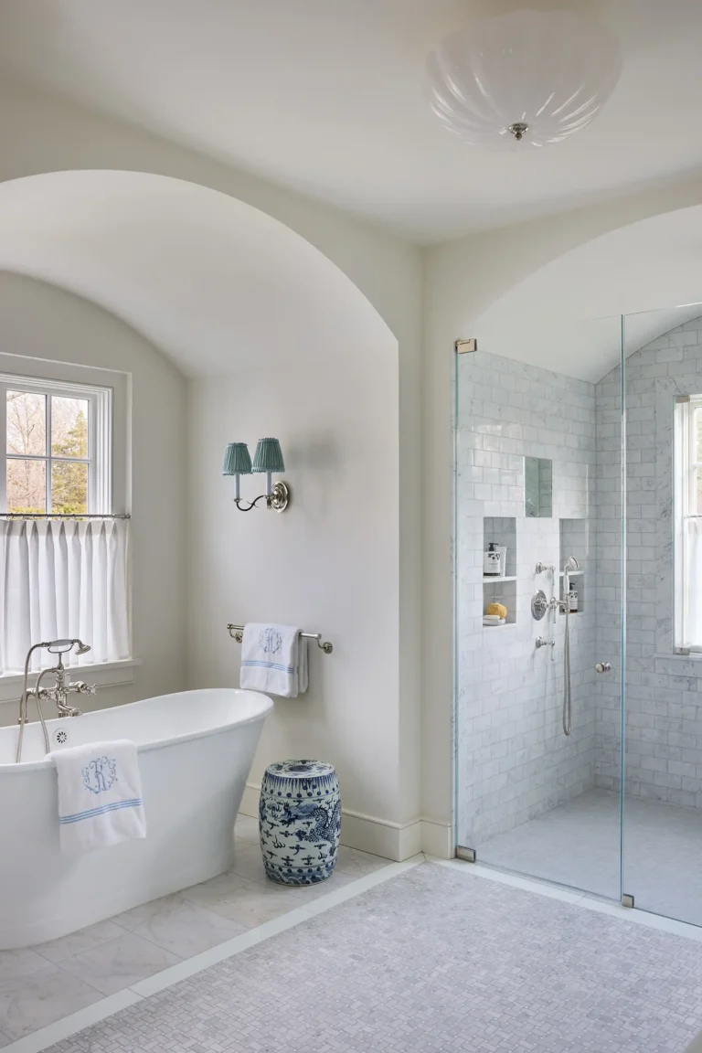 Primary bathroom with freestanding tub, arched opening, pale tile, glass shower, and window light