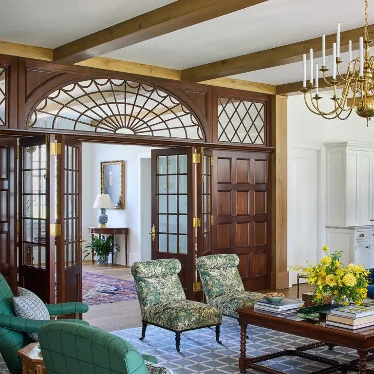 Living room in a Cape Dutch residence with mahogany screen, arched transom, patterned rug, chandelier, and view toward the entry hall