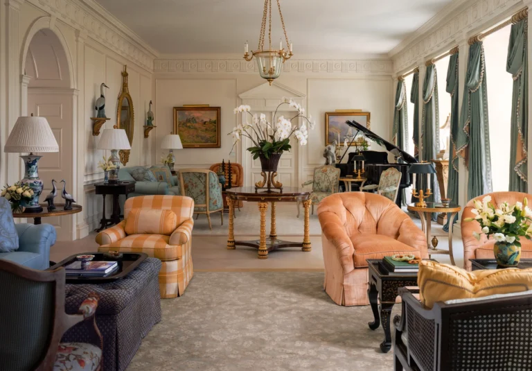 Formal Palm Beach living room with tall draped windows, pale walls, upholstered seating, chandelier, grand piano, and classical trim.
