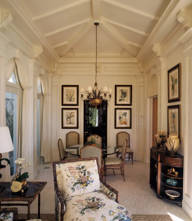 Bright sitting room with a vaulted coffered ceiling, arched windows, floral lounge chair, black cabinet, framed art, and classical trim.