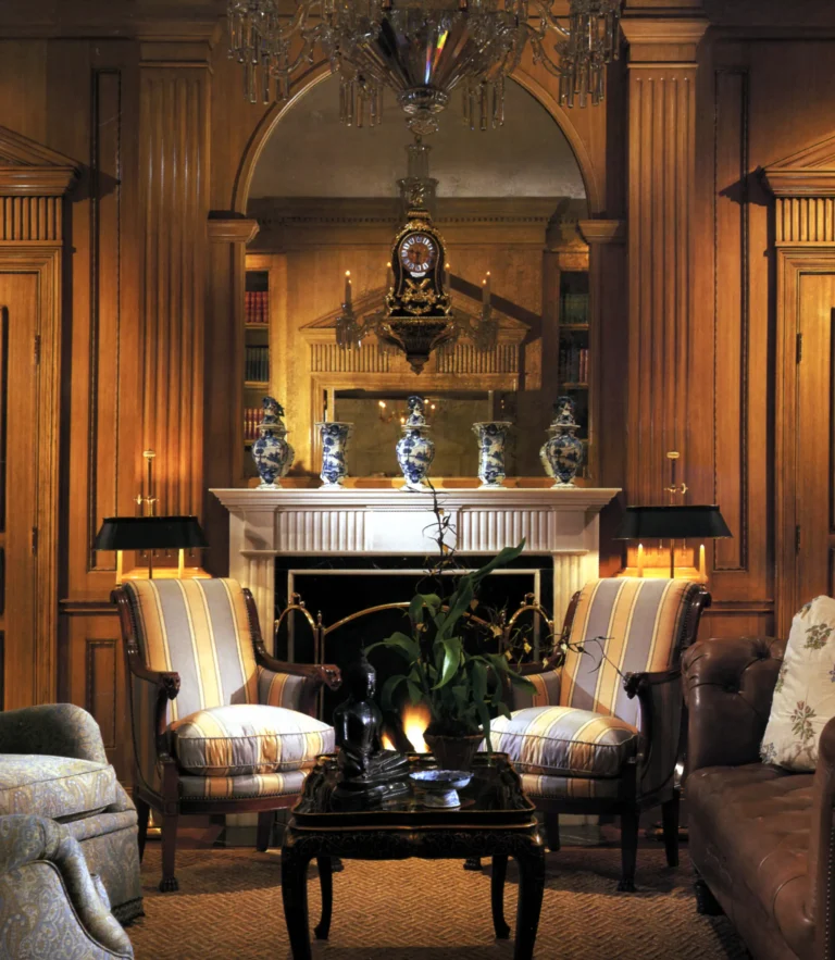 Paneled Palm Beach library with fireplace, built-in shelving, striped chairs, warm lighting, and classical pilaster detailing.