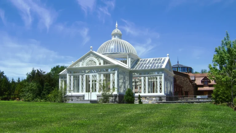 White glass conservatory at a Head of the Harbor estate retreat with a domed cupola, glazed roof, classical detailing, stone base, and lawn foreground.